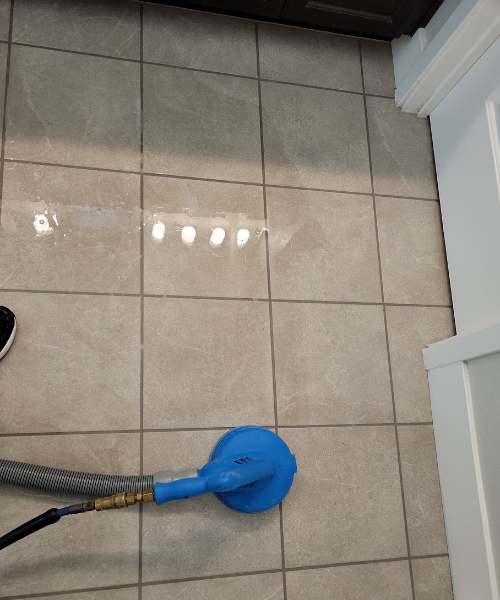 A person vacuuming a tile floor with a blue hose