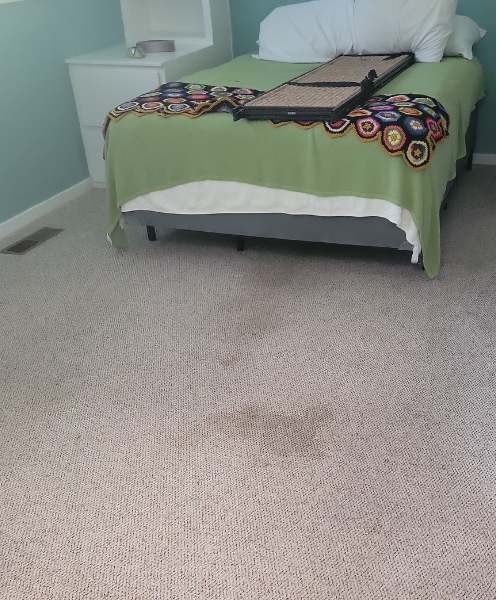 A bed with a green blanket and a white night stand