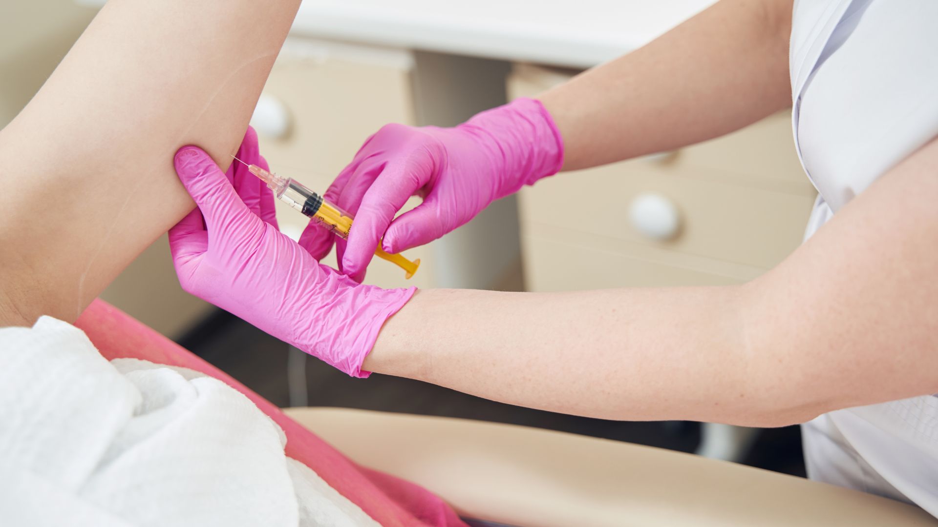 Medical professional in pink gloves administering an injection to patient's arm