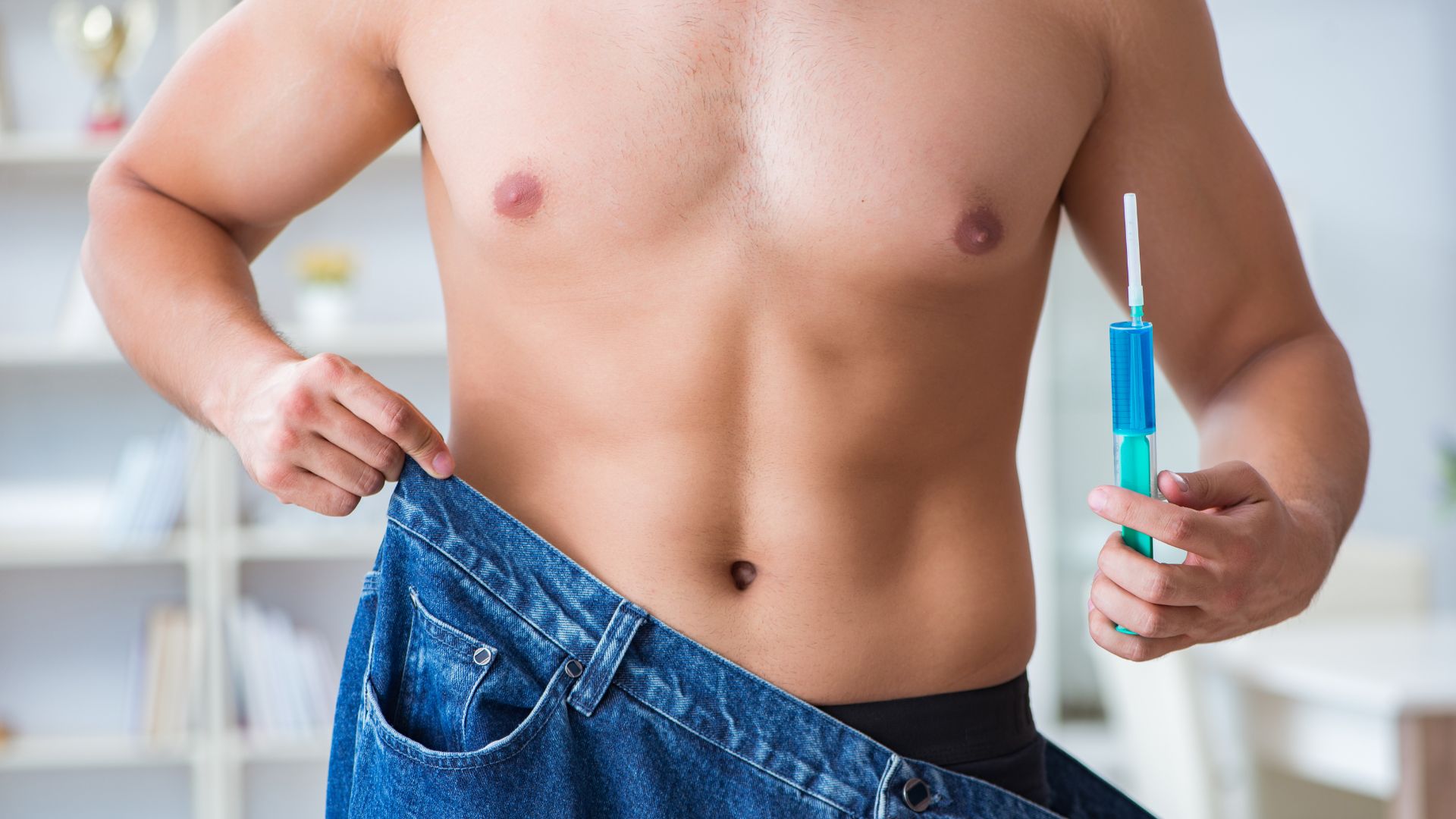 Muscular torso with loose jeans, holding blue medical syringe